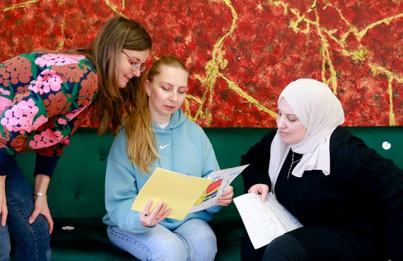 3 Frauen unterschiedlicher Herkunft sitzen auf einem Sfa und schauen gemeinsam in eine Broschüre